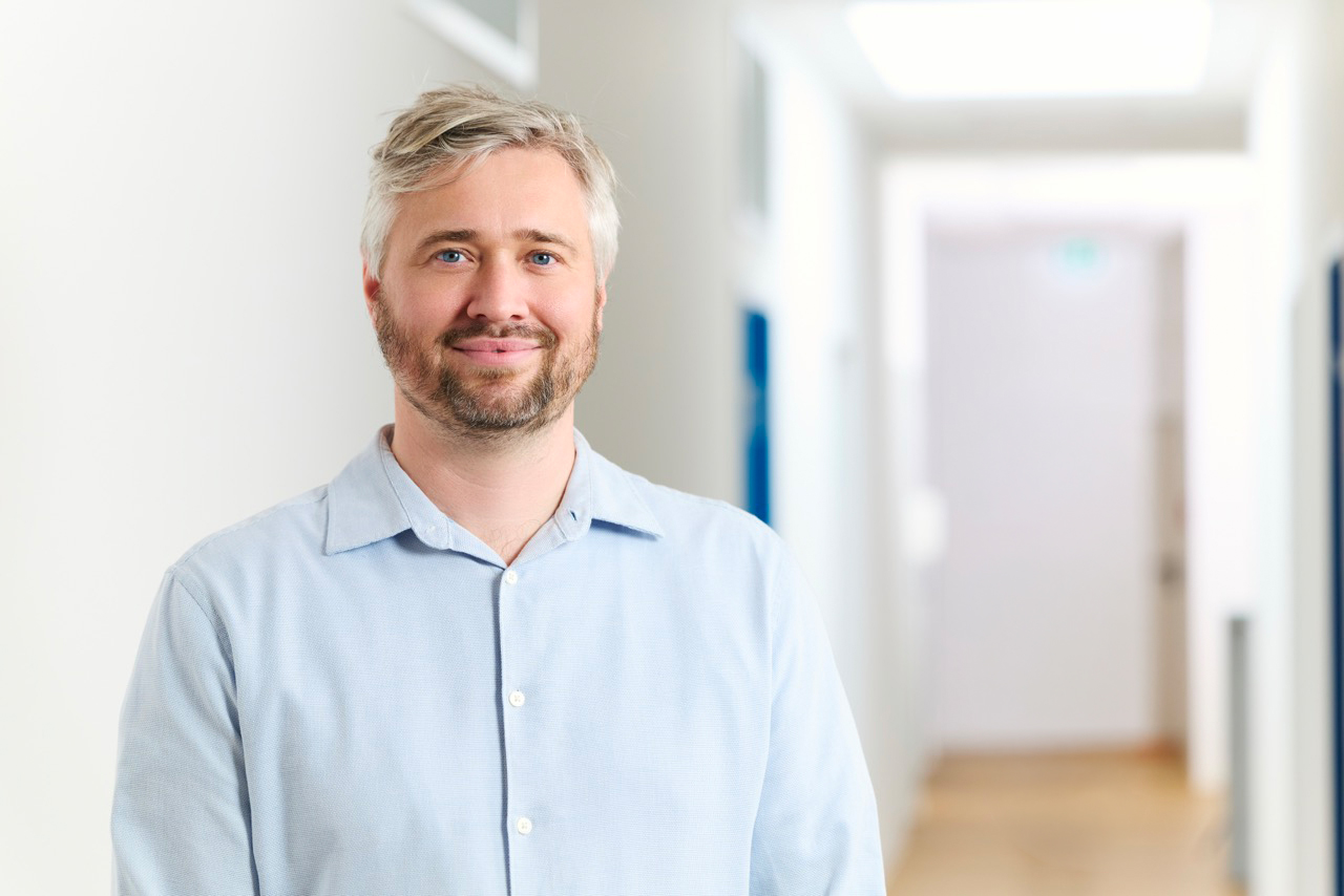 Porträt des lächelnden Arztes Benjamin Schwab in hellem Flur