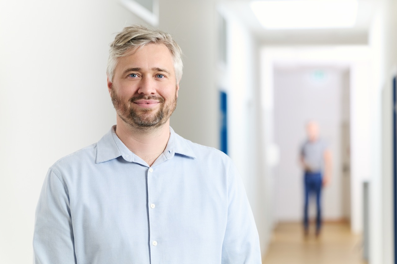 Porträt des lächelnden Arztes Benjamin Schwab in hellem Flur