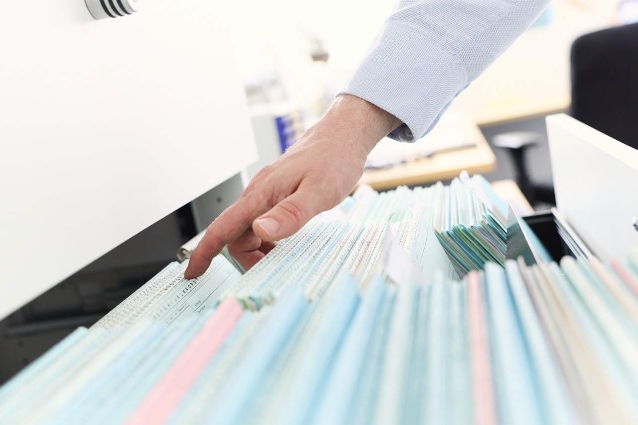 Hand zeigt auf eine Karteikarte zwischen Patientenakten
